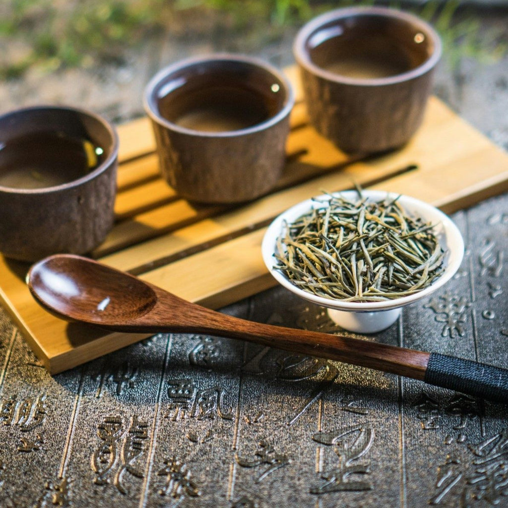 Three wooden cups with a small bowl of tea leaves on a textured surface.