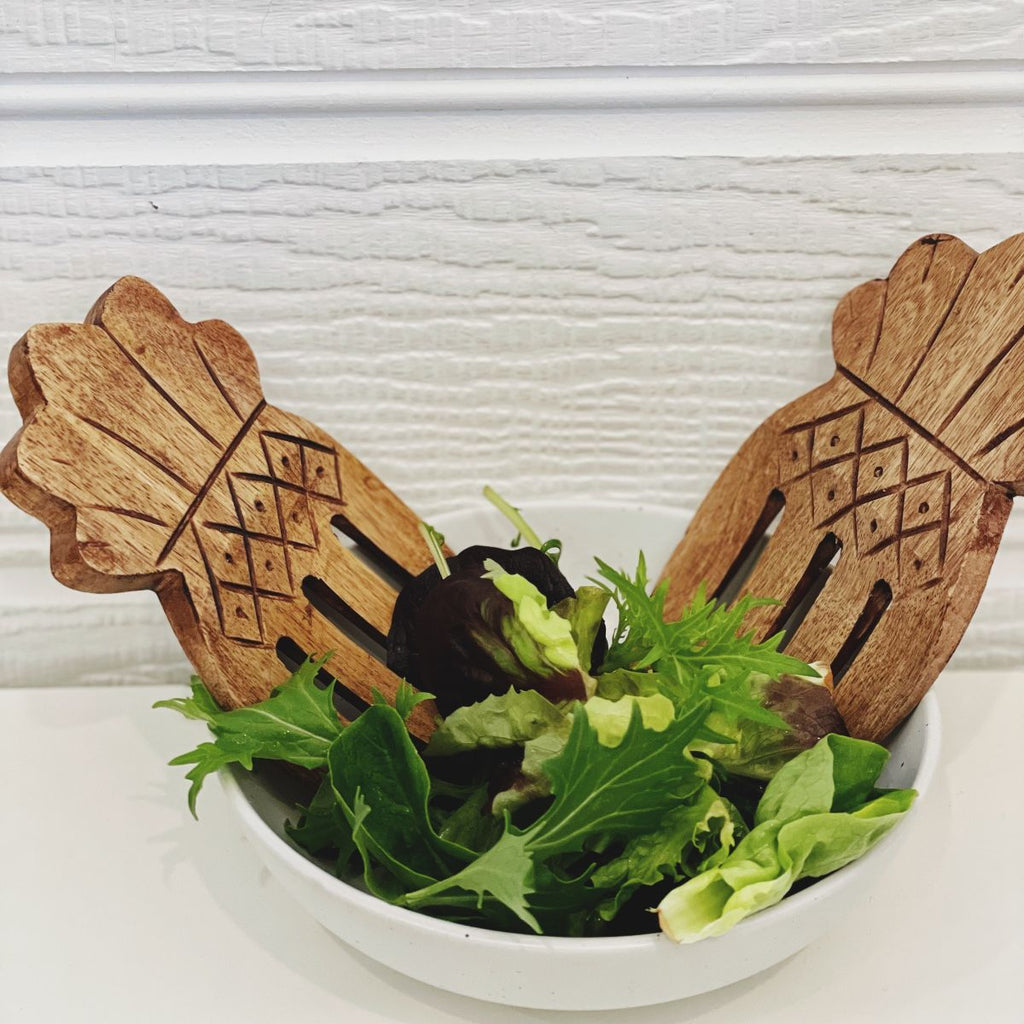 Wooden salad servers with pineapple design in a bowl of salad on a white background