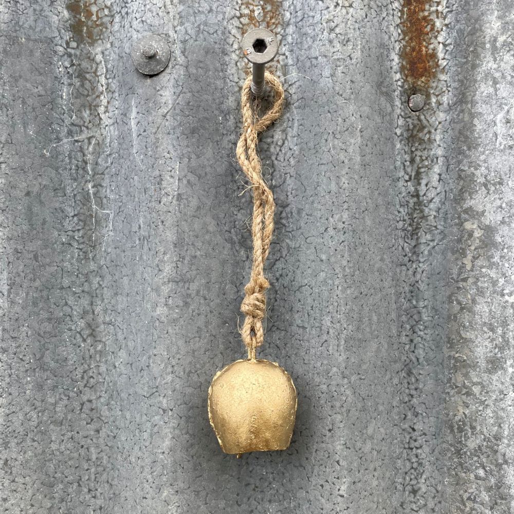 Mini Gold cow bell with jute rope attached to a textured metal surface