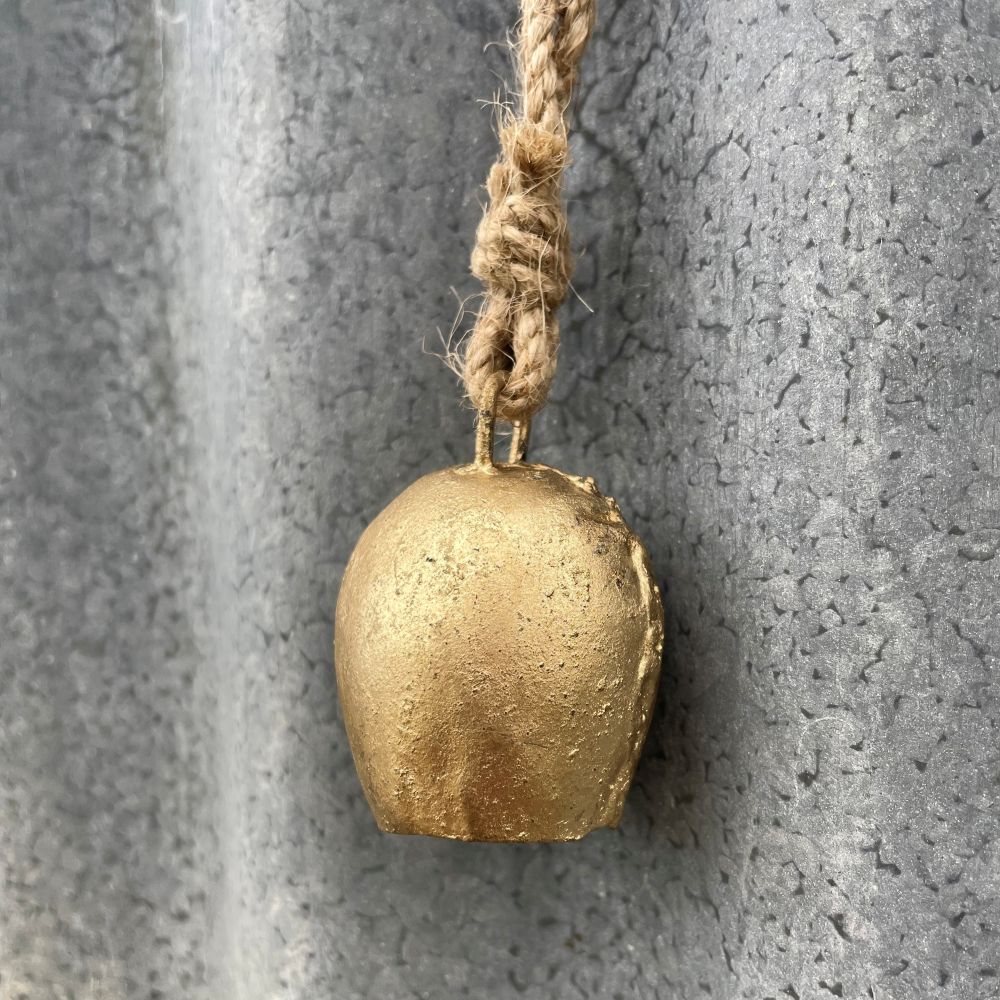Mini Gold cow bell with jute rope attached to a textured metal surface