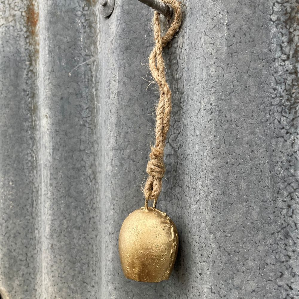Mini Gold cow bell with jute rope attached to a textured metal surface