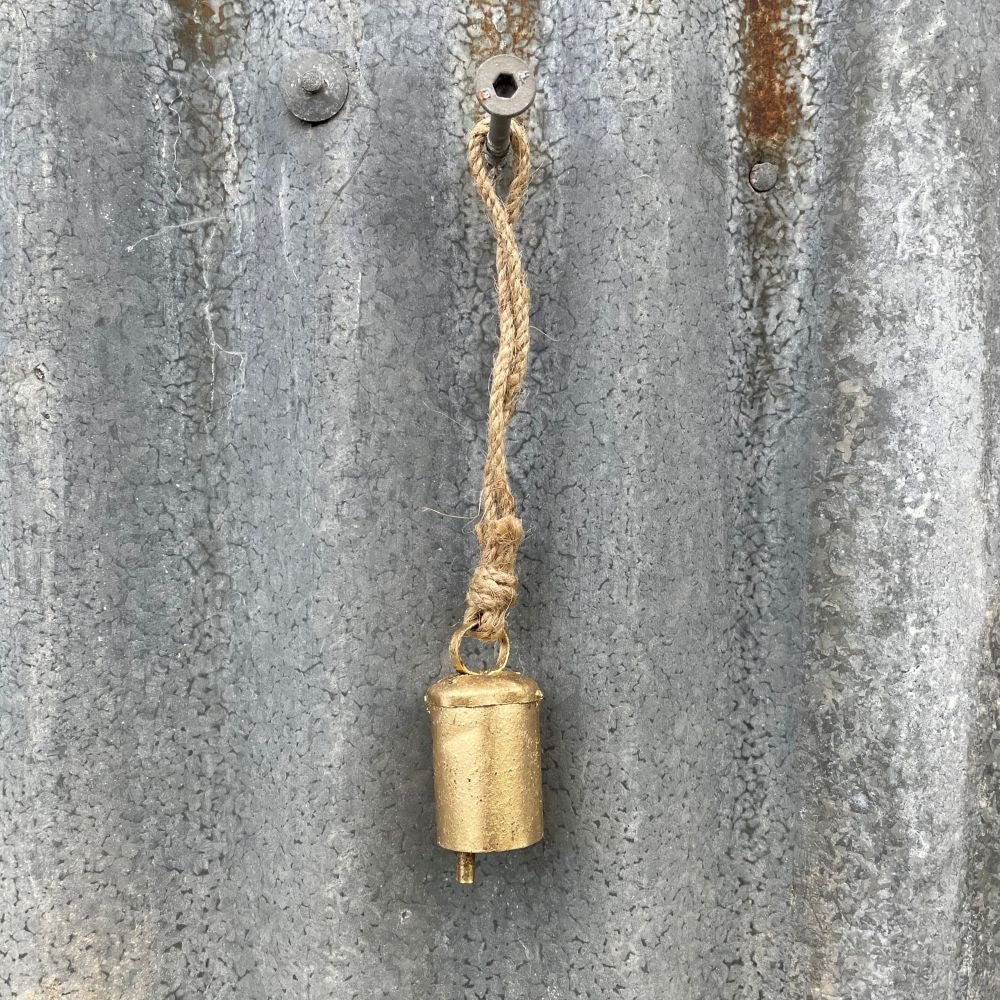 Mini Ages look brass bell hanging on a textured metal surface