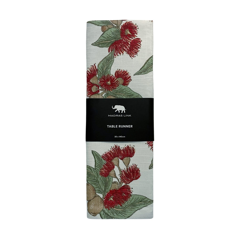 Folded fabric table runner in flowering gum pattern in red. green and brown on an off white base