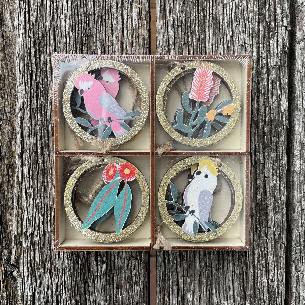 Set of eight decorative circular Christmas ornaments with Australiab birds and floral designs in a wooden box on a wooden background.