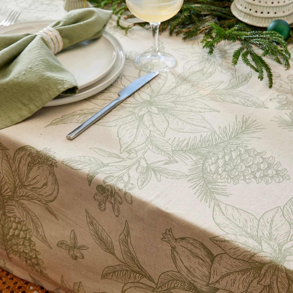 Table setting with a Poinsettia olive and flax tablecloth featuring pinecones and pomegranates, poinsettias and leaves.
