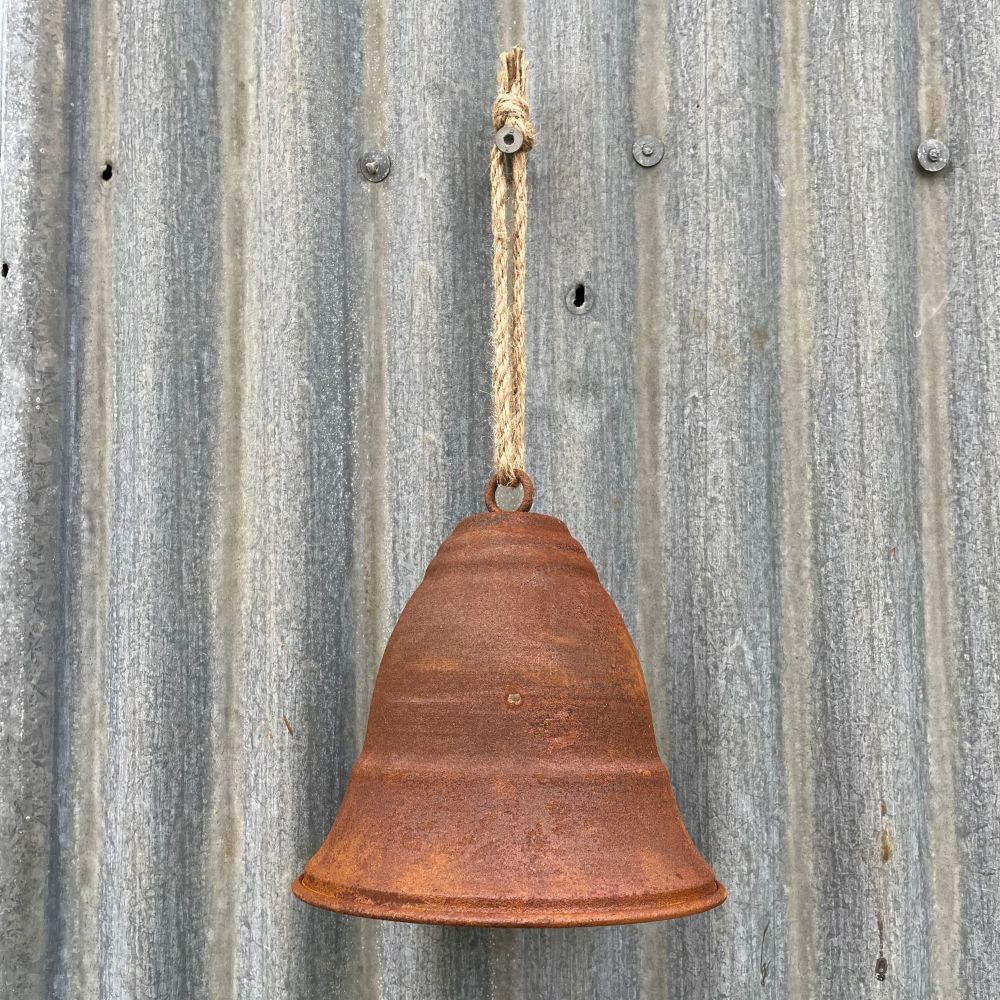 Rusty curved bell hanging on a corrugated metal wall