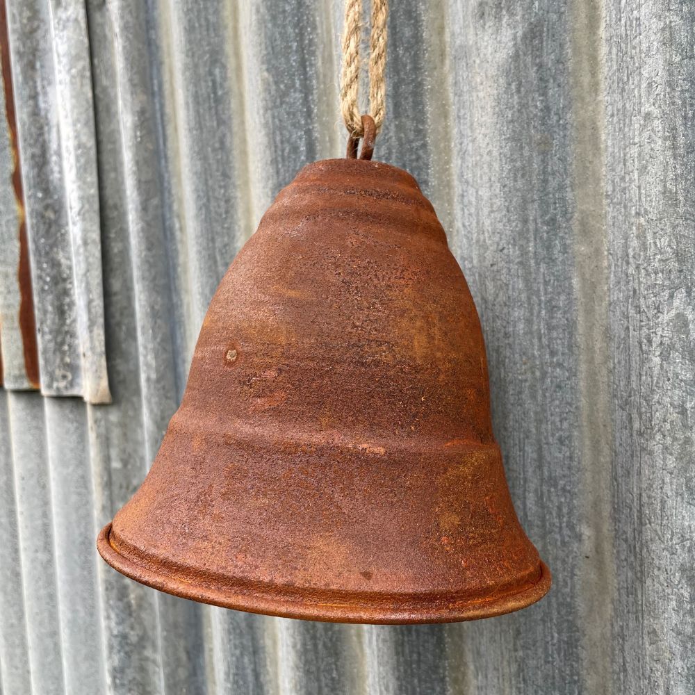 Rusty curved bell hanging on a corrugated metal wall - side angle