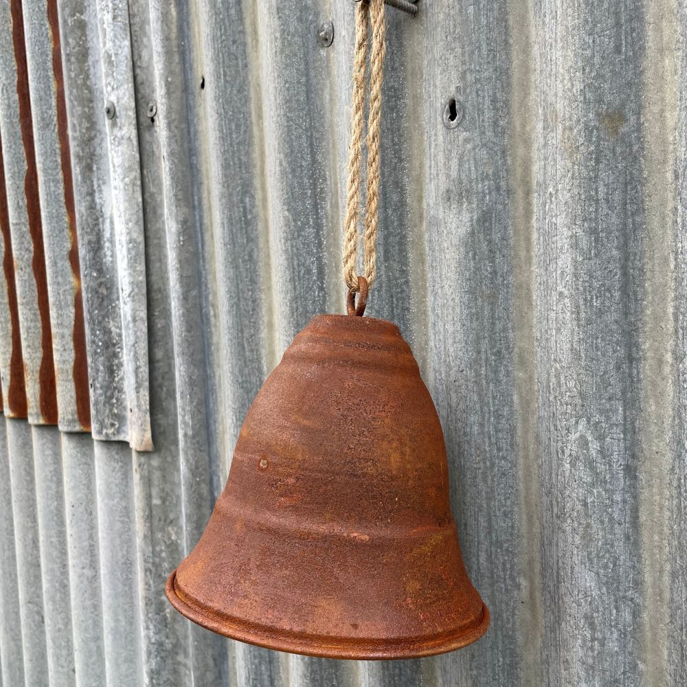 Rusty curved bell hanging on a corrugated metal wall - another angle