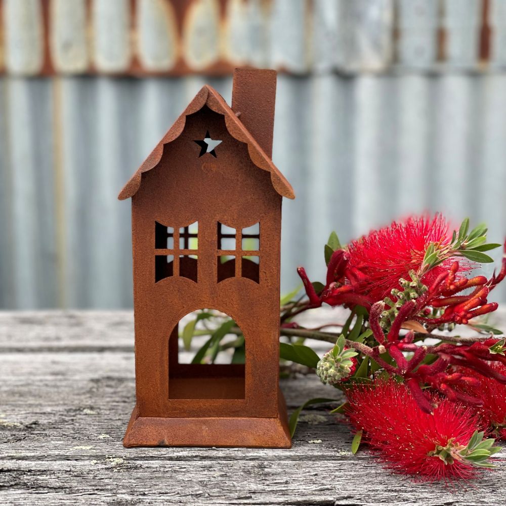 Rusty metal house shaped lantern or candle holder on a wooden table with an arrangement of Australian native flowers next to it