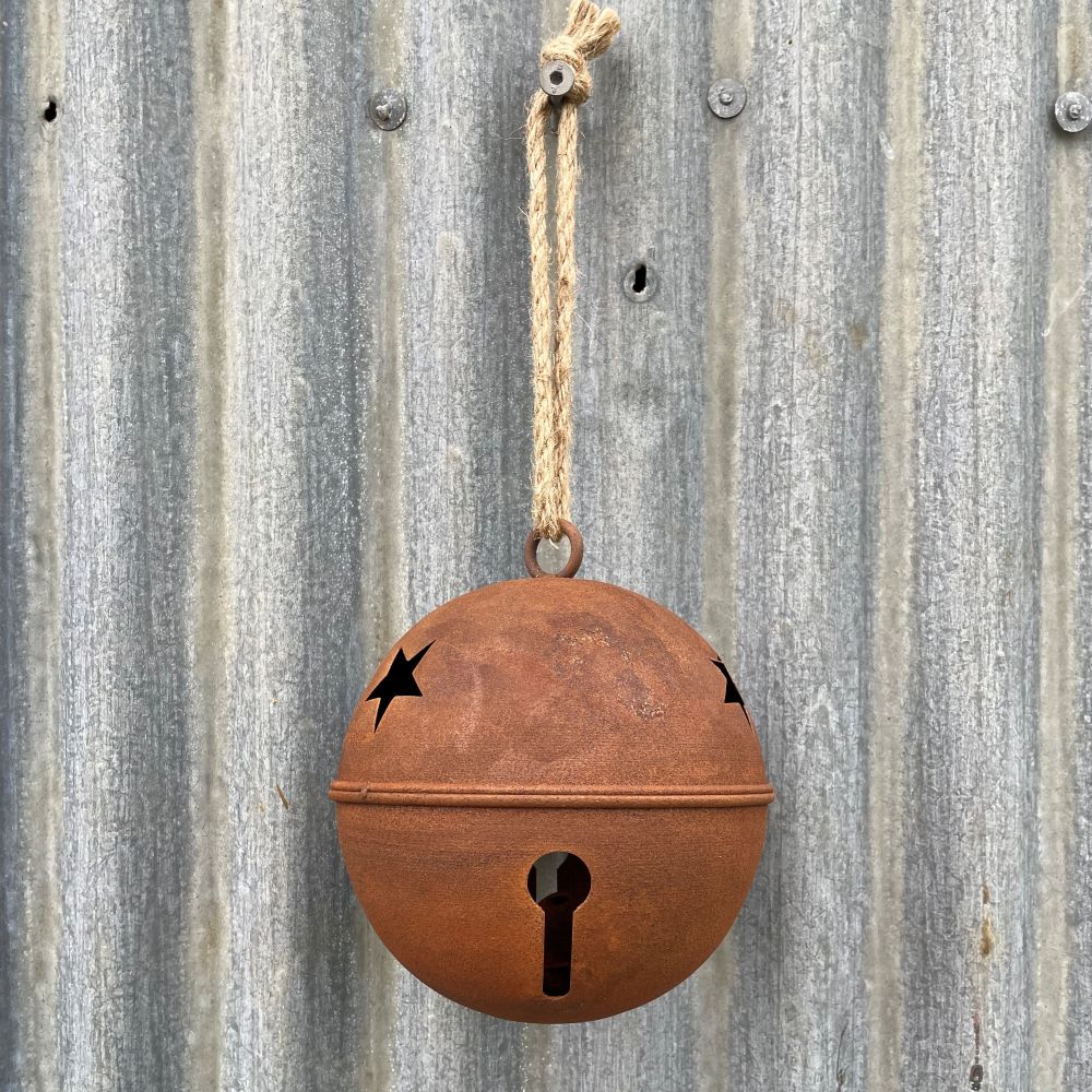 Rusty metal bell with cut-out stars hanging on a corrugated metal surface.