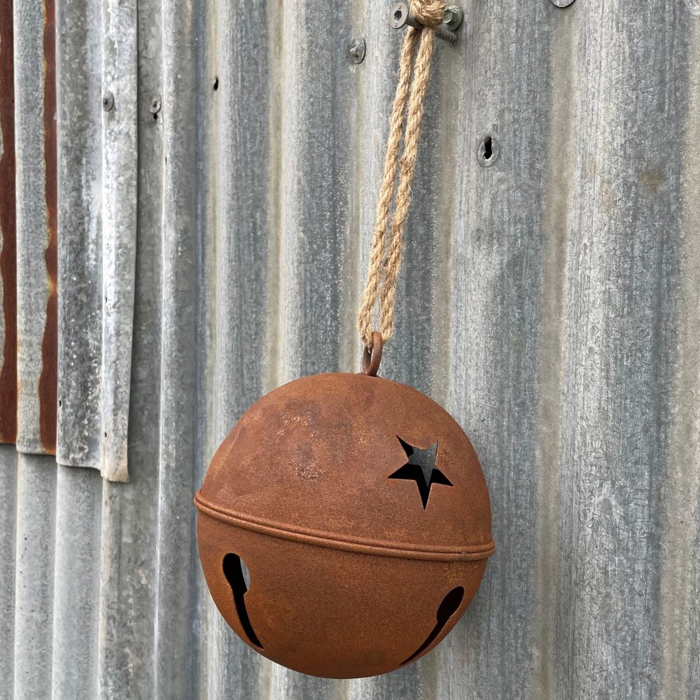 Rusty metal bell with cut-out stars hanging on a corrugated metal surface.