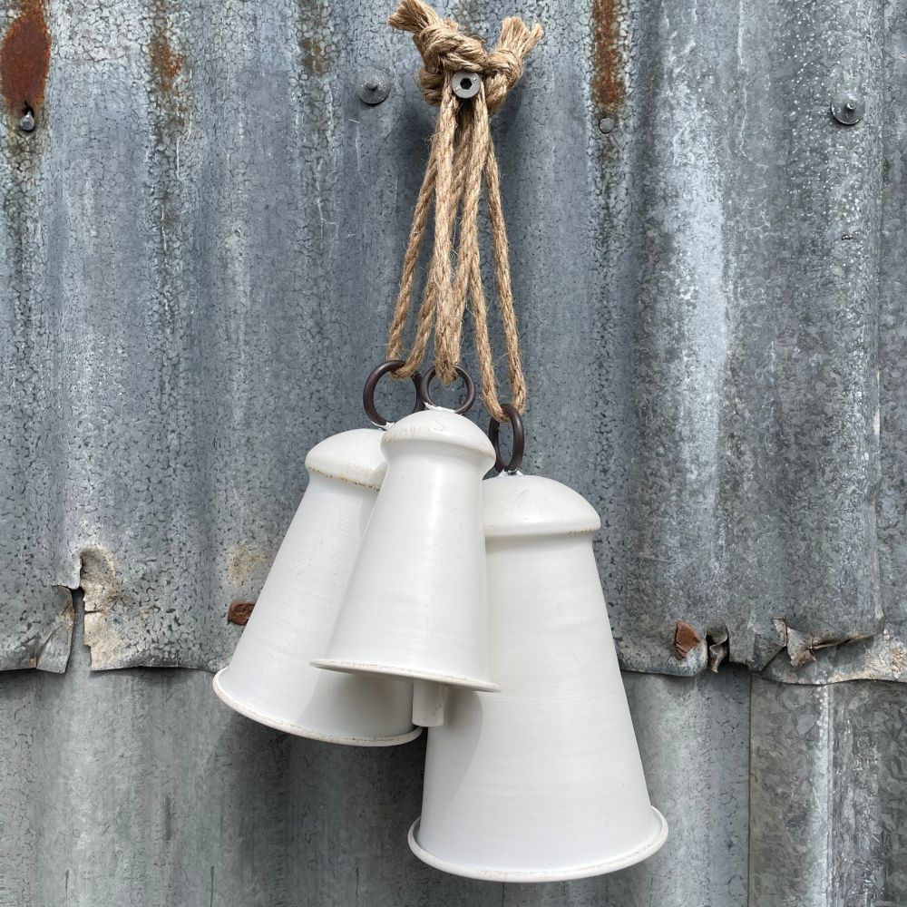 Set of 3 White bells in different sizes hanging on a rustic metal wall