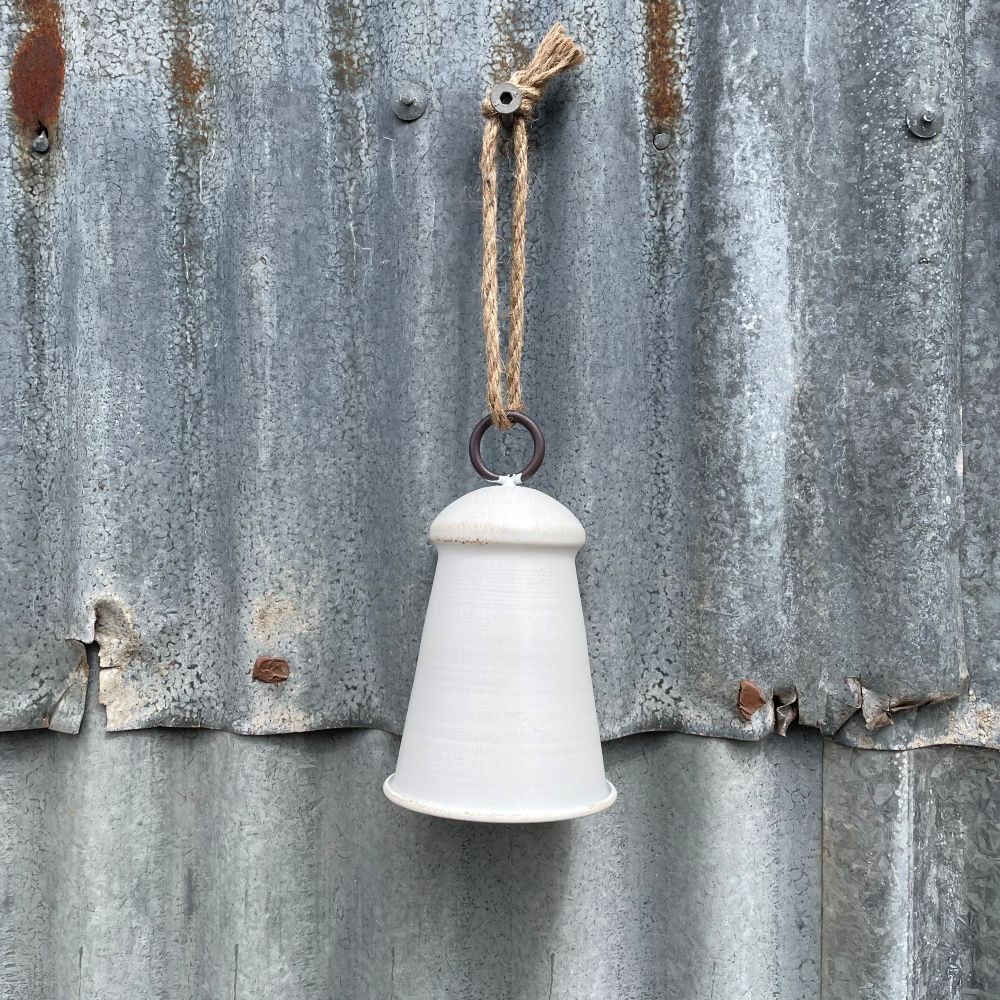Medium white/natural bell hanging on corrugated iron wall