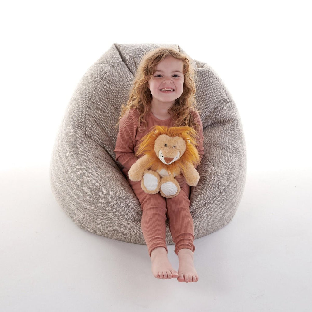 Child sitting on a bean bag chair holding a Snuggable Hottie plush lion toy against a white background