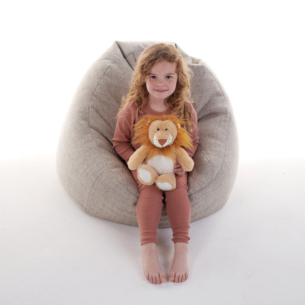 Child sitting on a bean bag holding a Snuggable Hottie plush lion toy against a white background