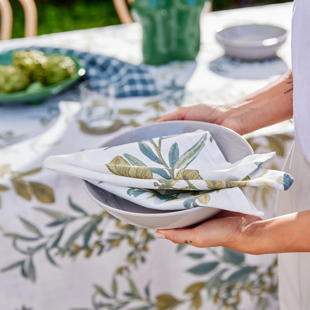 Person holding a stack of folded napkins with a leaf pattern on a table setting.
