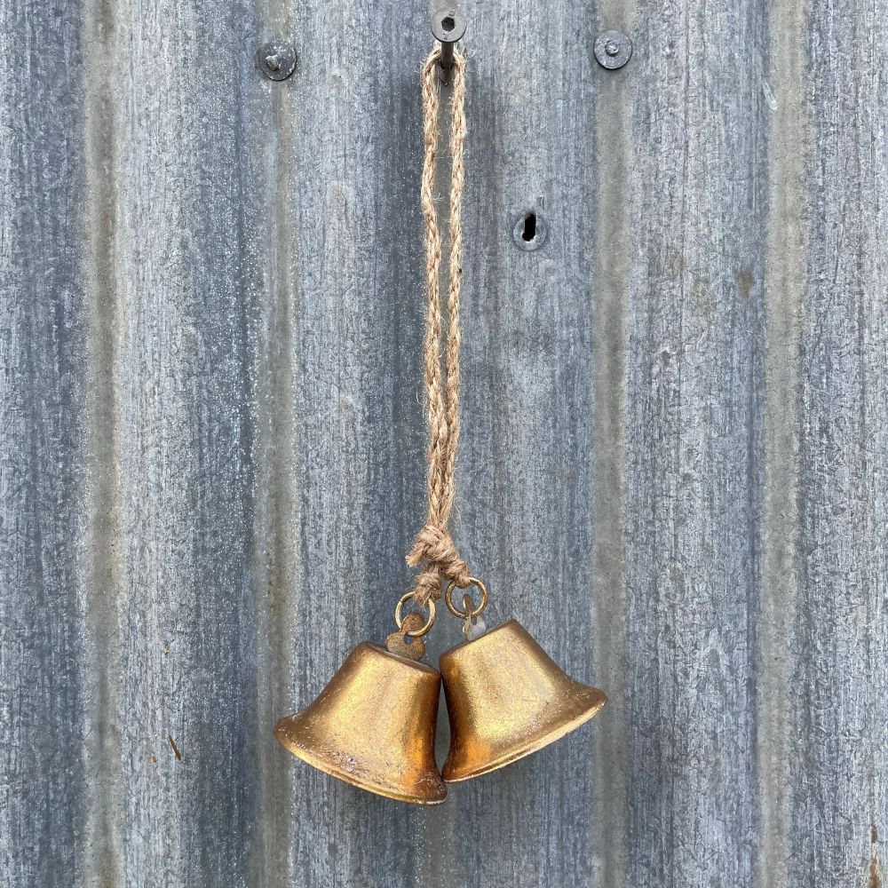 Pair of antique style brass bells hanging against a corrugated iron wall