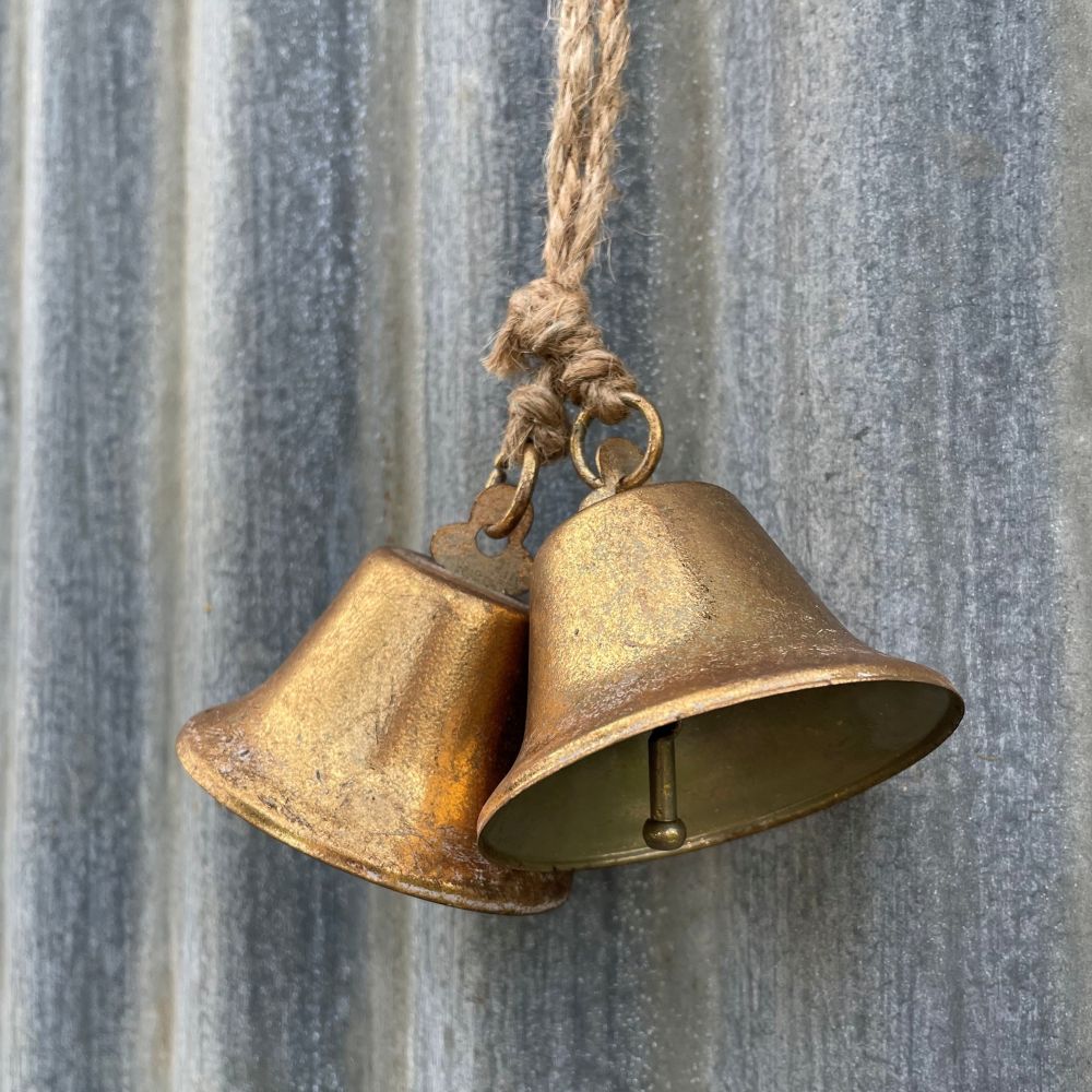 Pair of antique style brass bells hanging against a corrugated iron wall - other side angle