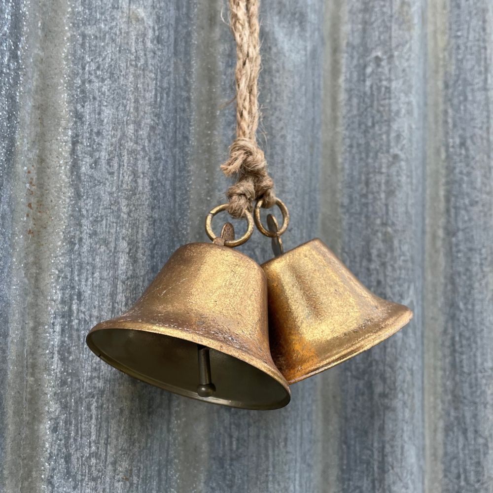 Pair of antique style brass bells hanging against a corrugated iron wall - side angle
