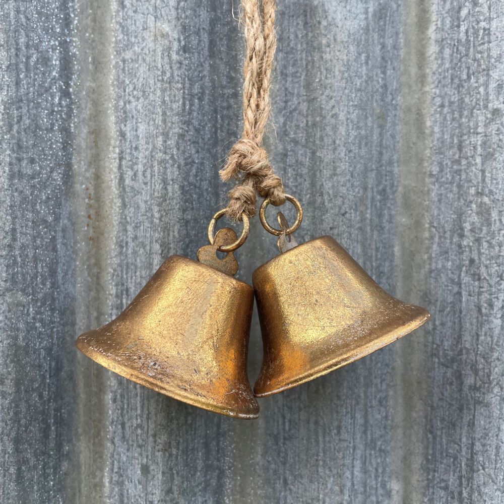 Pair of antique style brass bells hanging against a corrugated iron wall