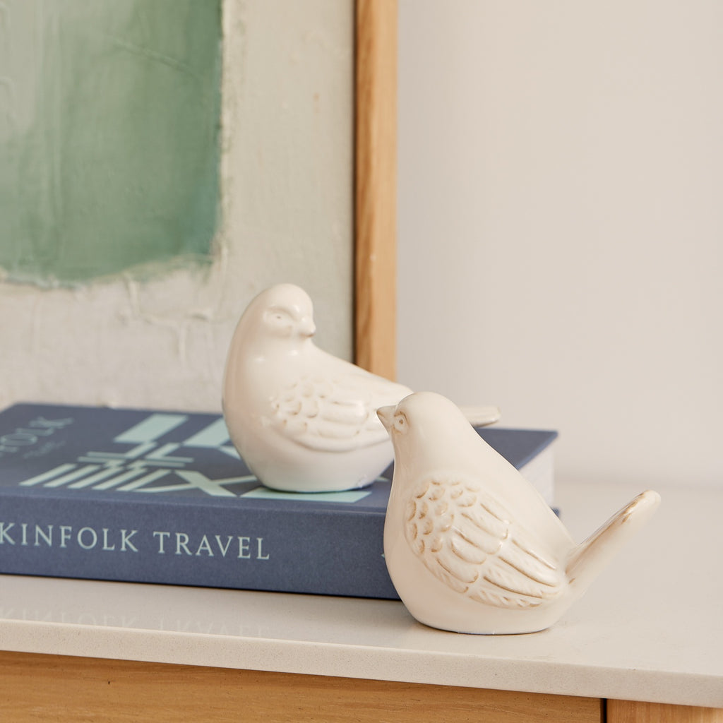 Twig and Feather - Two off white ceramic birds styled on a blue book with a print in the background - by Madras Link