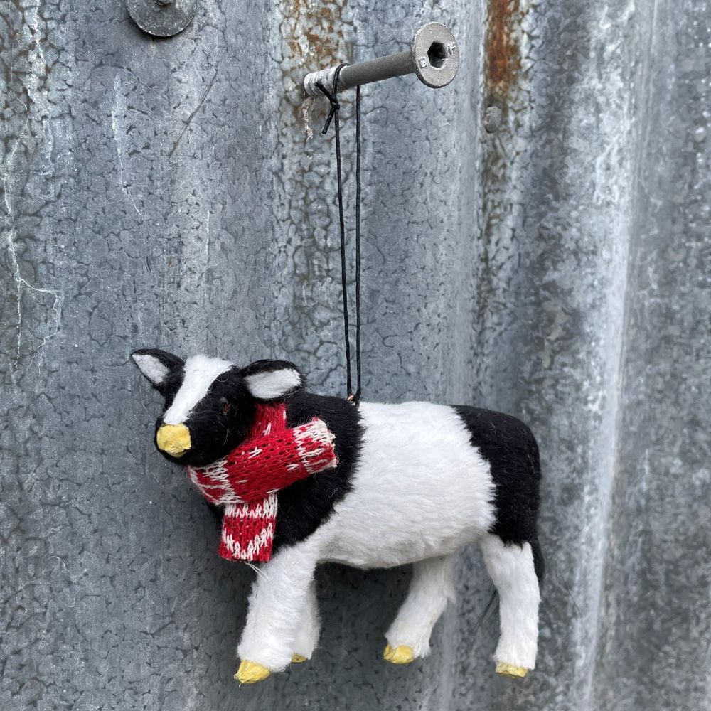 Small black and white cow ornament wearing a red scarf on a textured metal surface - more detail