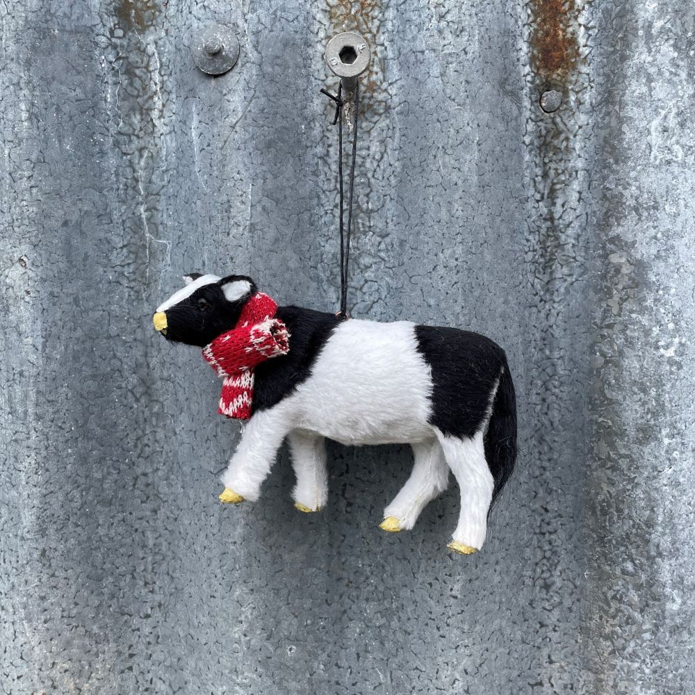 Small black and white cow ornament wearing a red scarf on a textured metal surface