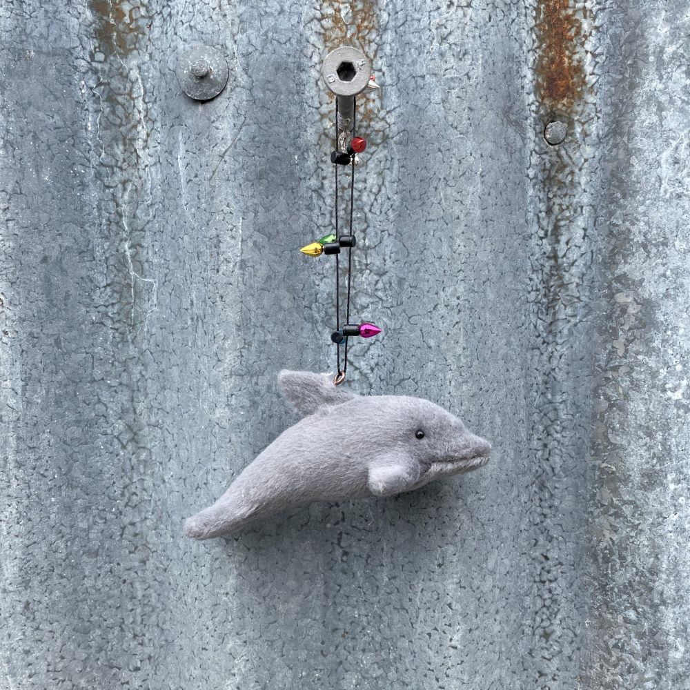 Small gray dolphin ornament with light garland on a textured metal surface
