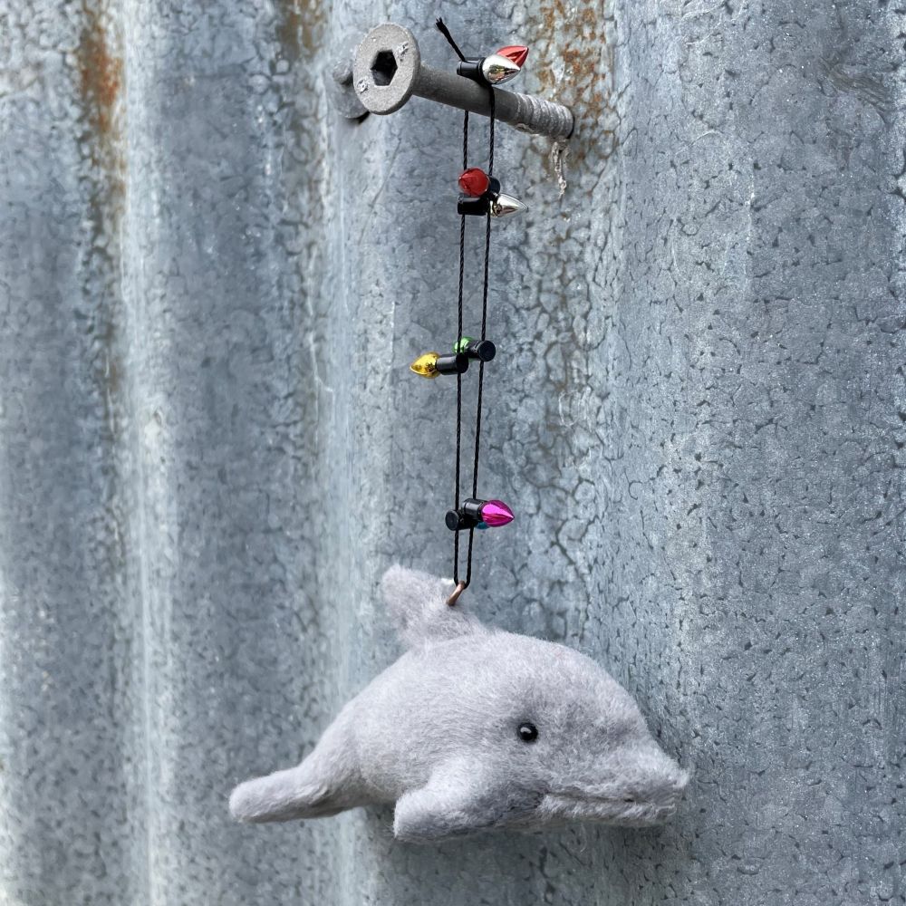 Small gray dolphin ornament with light garland on a textured metal surface - more detail