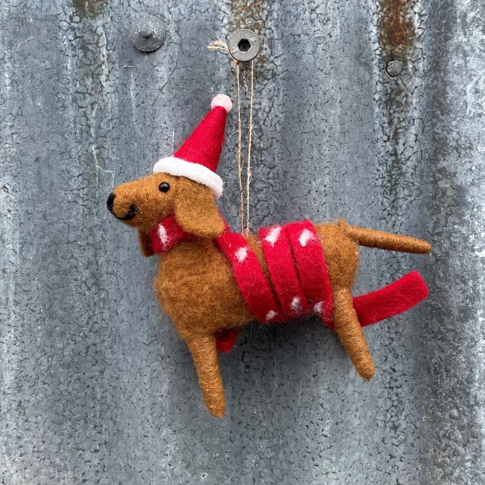 Brown felt dog with red and white scarf and hat hanging on a corrugated iron wall