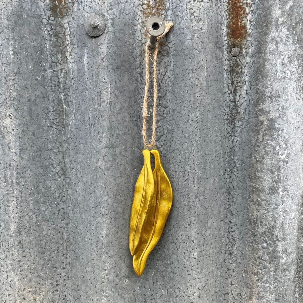 Gold leaf-shaped ornament hanging on a textured metal surface