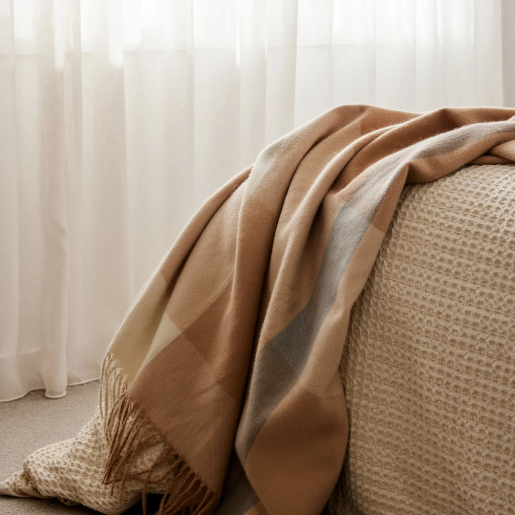 Harley charcoal Beige/neutral check throw rug draped over a textured surface with white curtains in the background