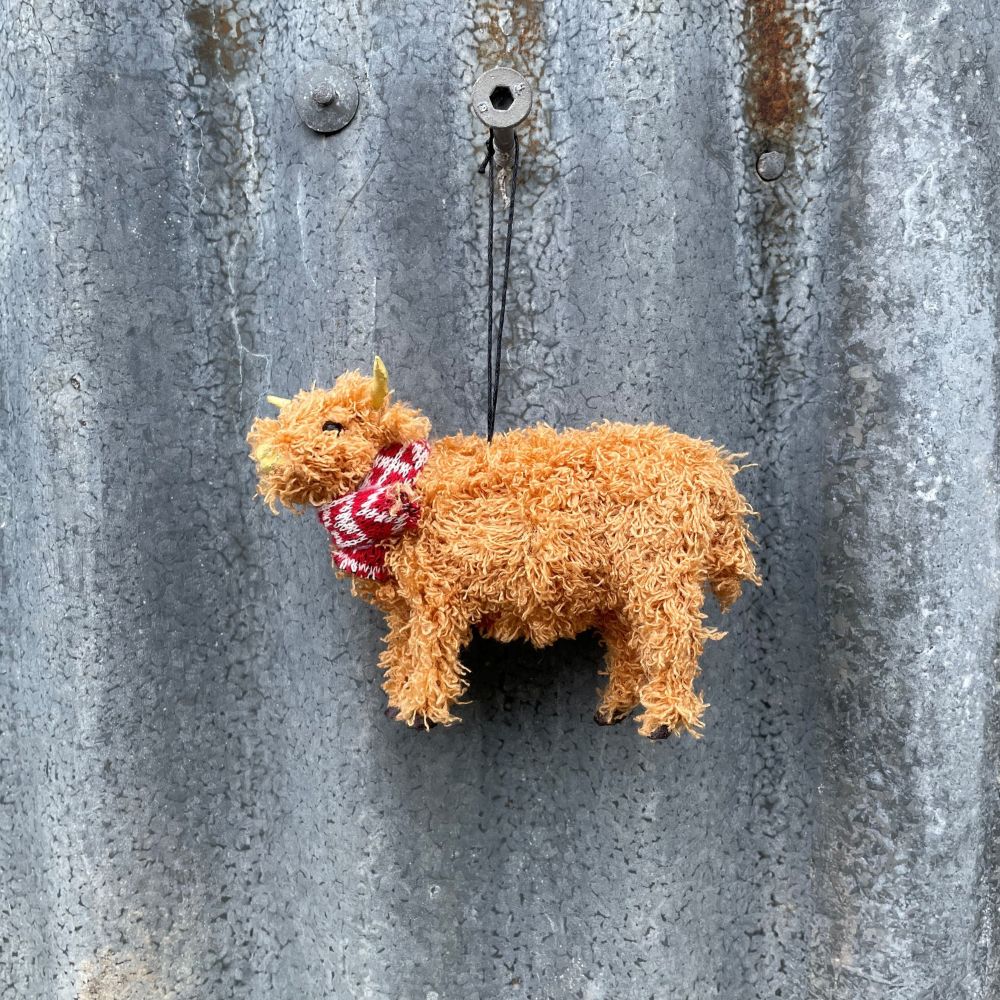 Christmas highland cow with a red and white patterned tie hanging on a metal wall.