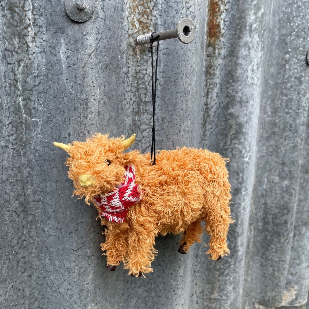Christmas highland cow with a red and white patterned tie hanging on a metal wall.