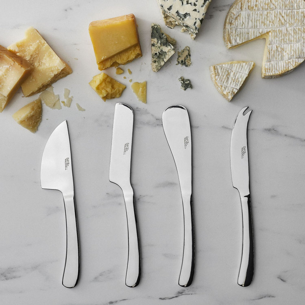 Set of four Kingsley stainless steel cheese knives on a marble surface with various types of cheese.