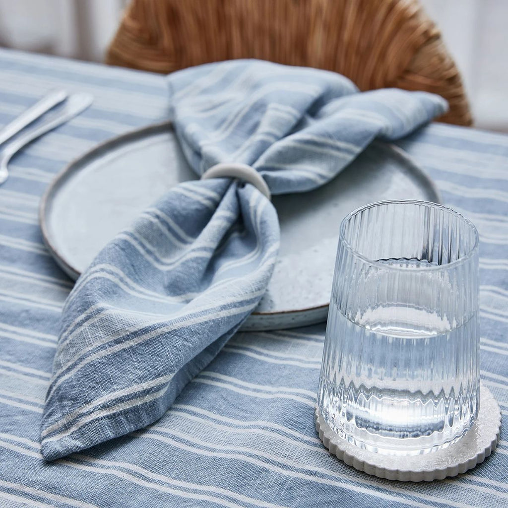 Glass of water on a coaster with a blue striped napkin on a plate