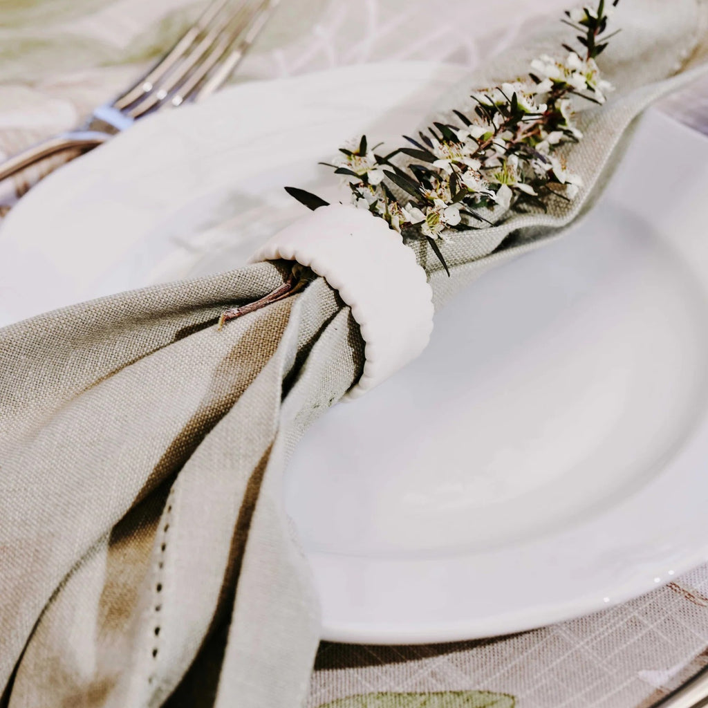 Close-up of a neatly rolled up mineral green napkin in a napkin ring with a floral decoration on a white plate.