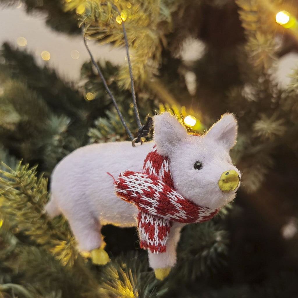 Pink pig ornament with a red and white scarf on a Christmas tree.