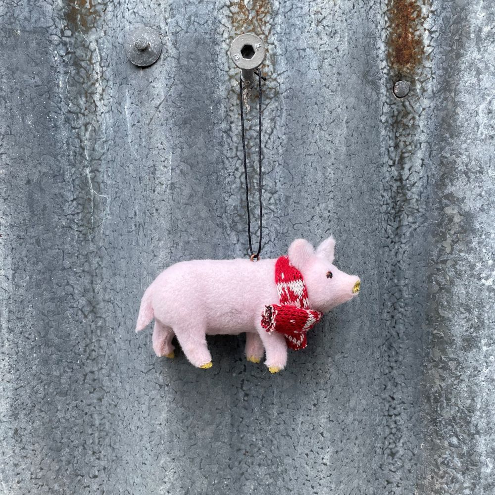 Small pink pig ornament with a red scarf hanging on a textured metal surface