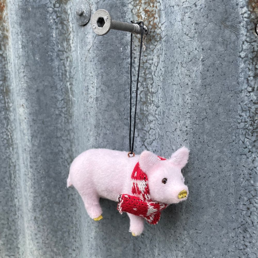 Small pink pig ornament with a red scarf hanging on a textured metal surface