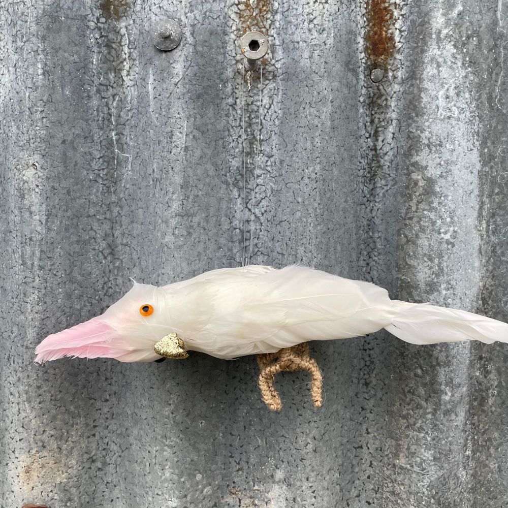Pinky cockatoo hanging decoration with feathers and a glitter beak - on a textured metal surface