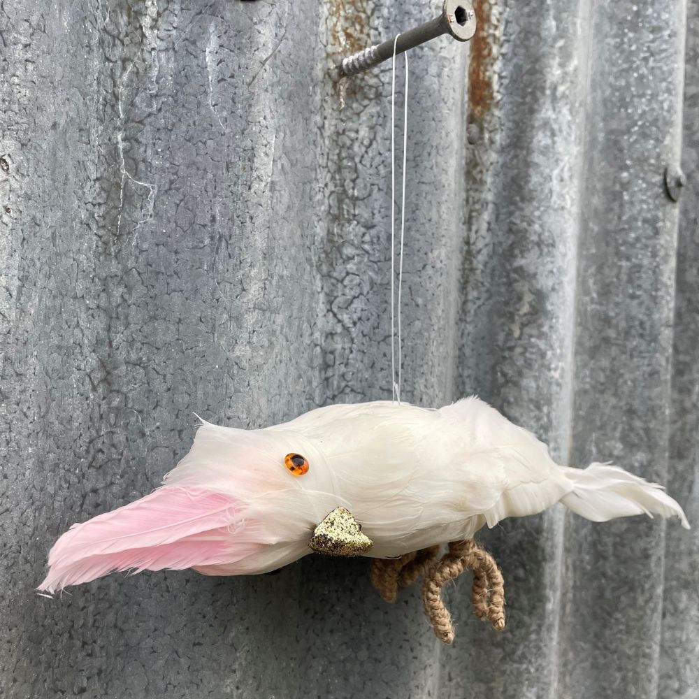 Pinky cockatoo hanging decoration with feathers and a glitter beak - on a textured metal surface