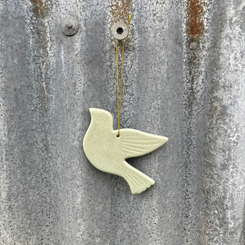 Ceramic dove ornament in soft sage green hanging on a textured metal surface