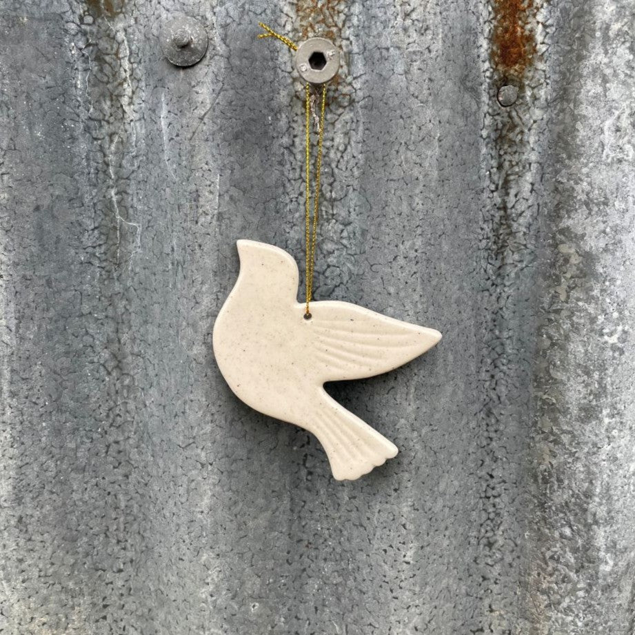 White ceramic dove ornament hanging on a textured metal surface