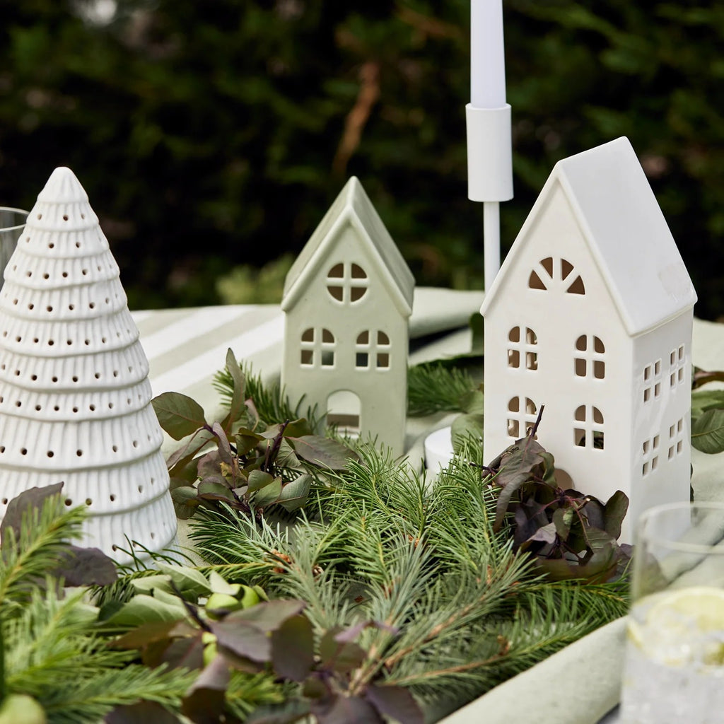 Decorative white ceramic houses and tree with greenery on a table