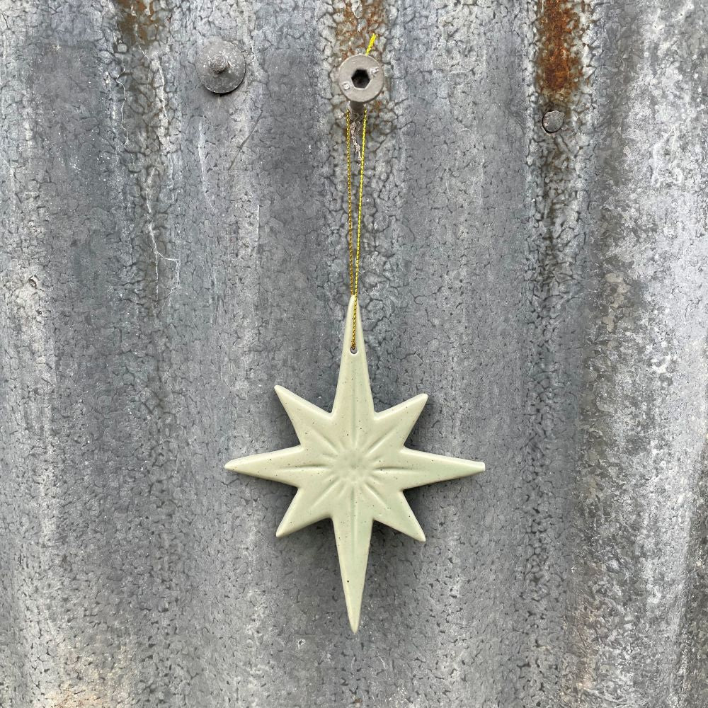 Decorative ceramic star in soft sage green hanging on a textured metal surface