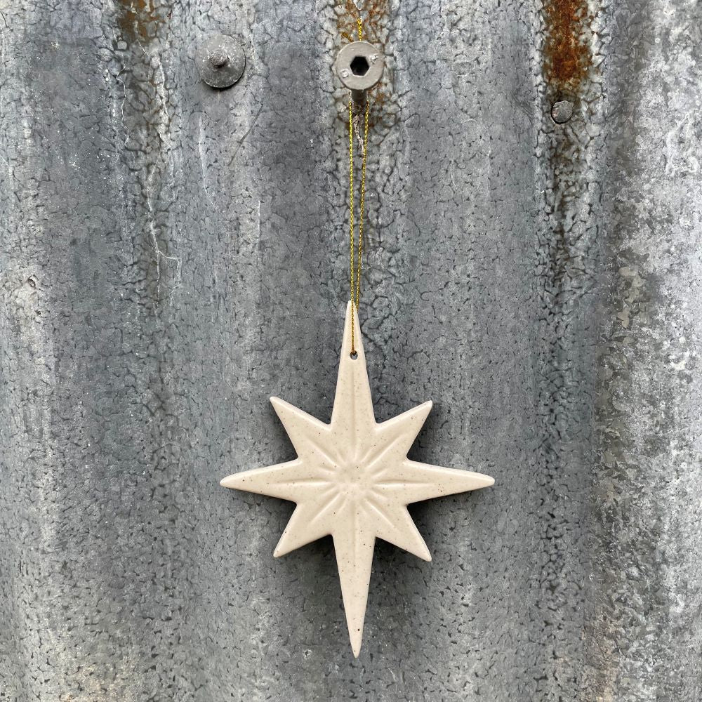 White star-shaped ceramic ornament hanging on a textured metal surface