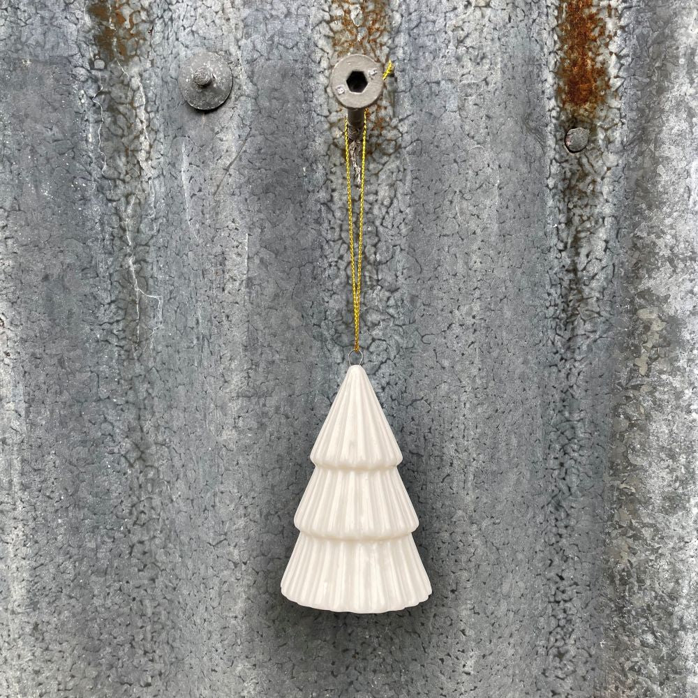 White ceramic Christmas tree ornament hanging on a textured metal wall.