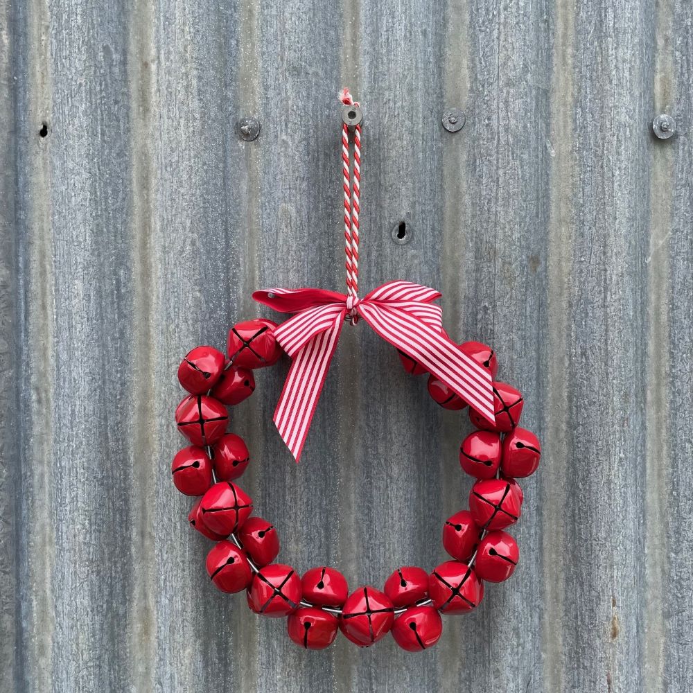 Red bell wreath with a red and white striped ribbon hanging on a corrugated metal surface.
