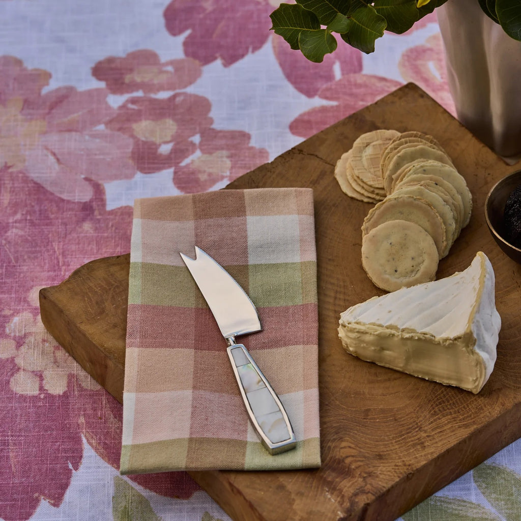 Rosie Check napkins with Cheese platter with a wedge of cheese, crackers, and a cheese knife on a wooden board with a floral tablecloth.